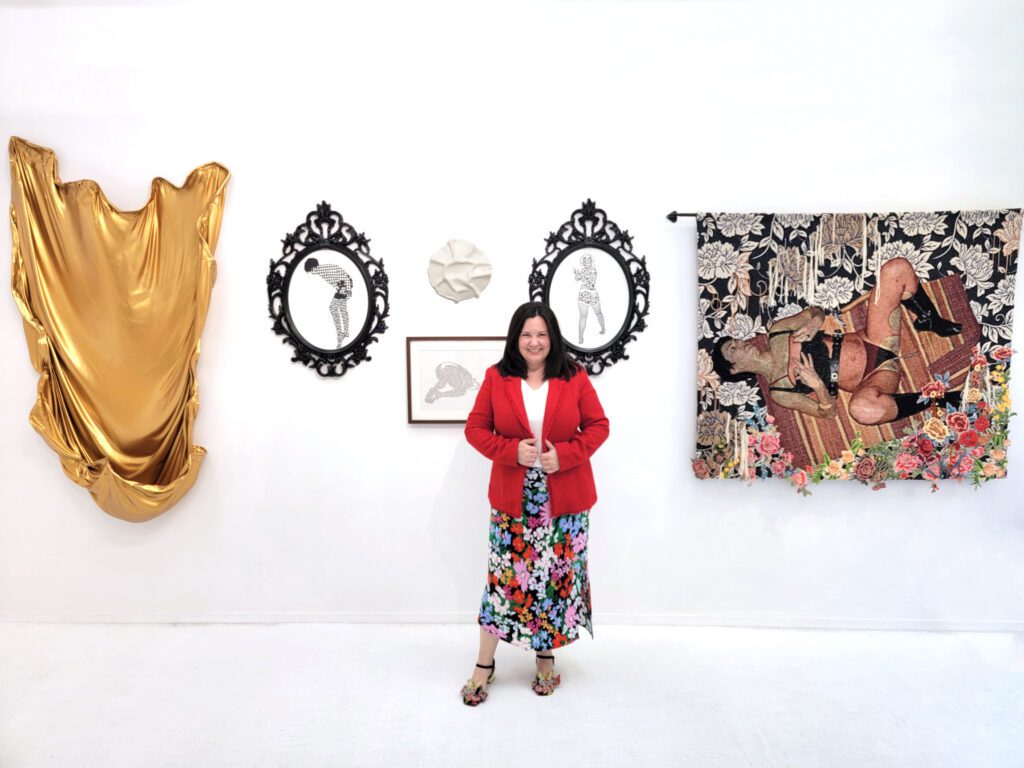 Curator Erica Criss in her exhibition "Womanhood 102" (with Lesley Bodzy’s "Soft Embrace I," 2022. Acrylic. 69 x 43 x 11 inches, on the left and works by Katie Commodore in the middle and on the right). Courtesy of the curator.