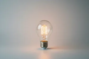 Glowing LED light bulb on a soft gray background, symbolizing an easy first step to cut energy use and carbon footprint.