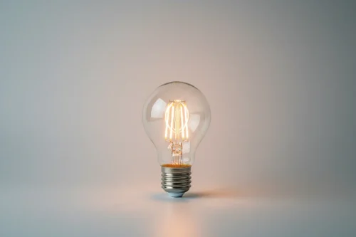 Glowing LED light bulb on a soft gray background, symbolizing an easy first step to cut energy use and carbon footprint.